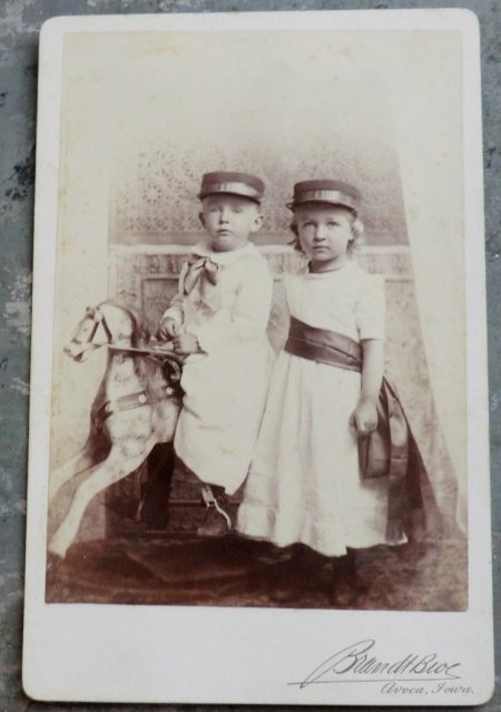 Старинная фотография, изображающая мальчика на лошадке-качалке и девочку